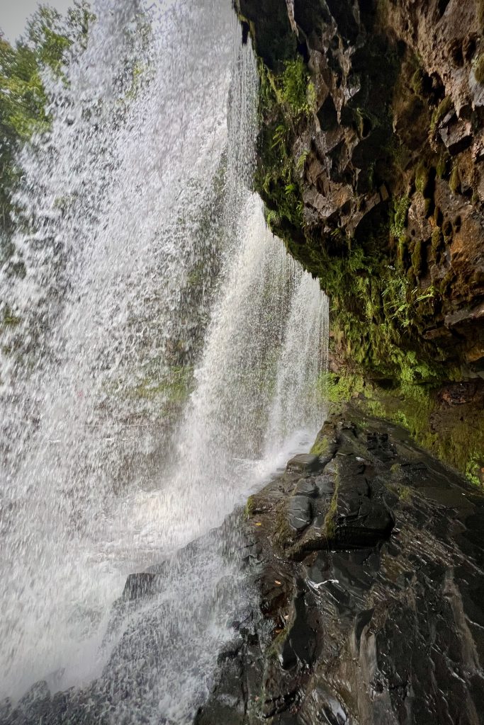 Lopen achter de waterval Sgwd yr Eira in Waterfall Country, Bannau Brycheiniog National Park, Wales.