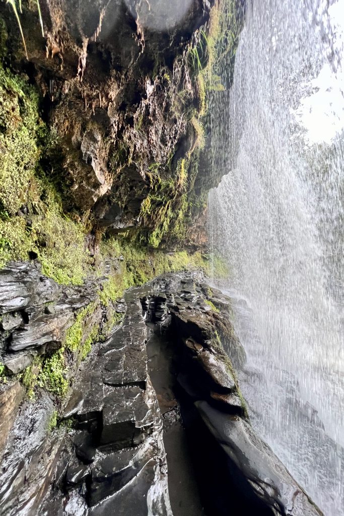Lopen achter de waterval Sgwd yr Eira in Waterfall Country, Bannau Brycheiniog National Park, Wales.