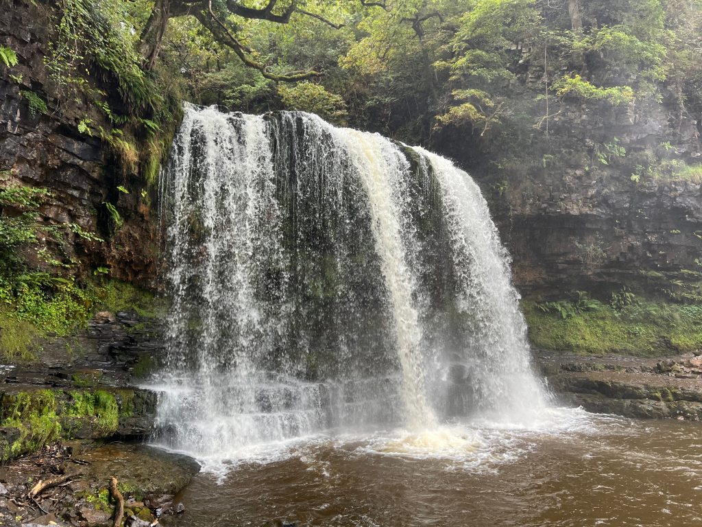 Lopen achter de waterval Sgwd yr Eira in Waterfall Country, Bannau Brycheiniog National Park, Wales.